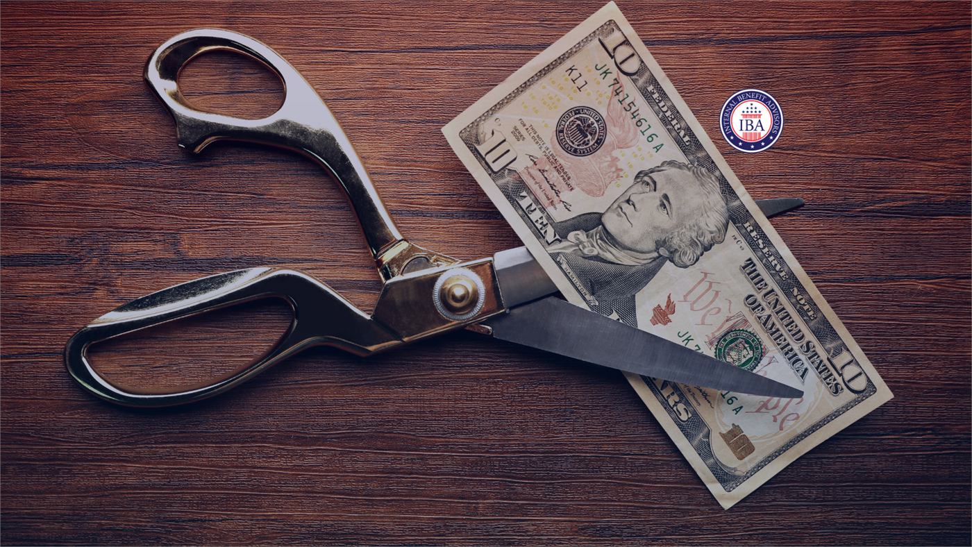 A large pair of scissors cutting through a ten dollar bill on a dark wooden surface