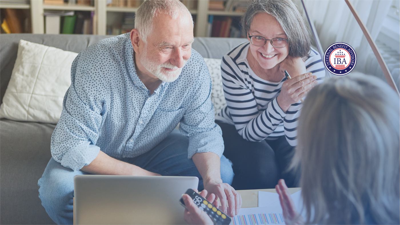 An older couple smiling over a laptop while an adviser, seen from behind, talks them through a document