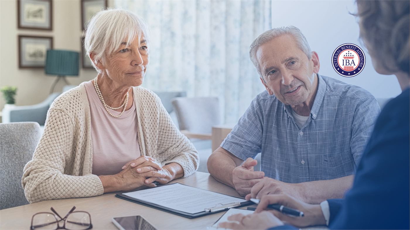 An older couple at a table with paperwork in front of them, listening to an adviser seen from behind