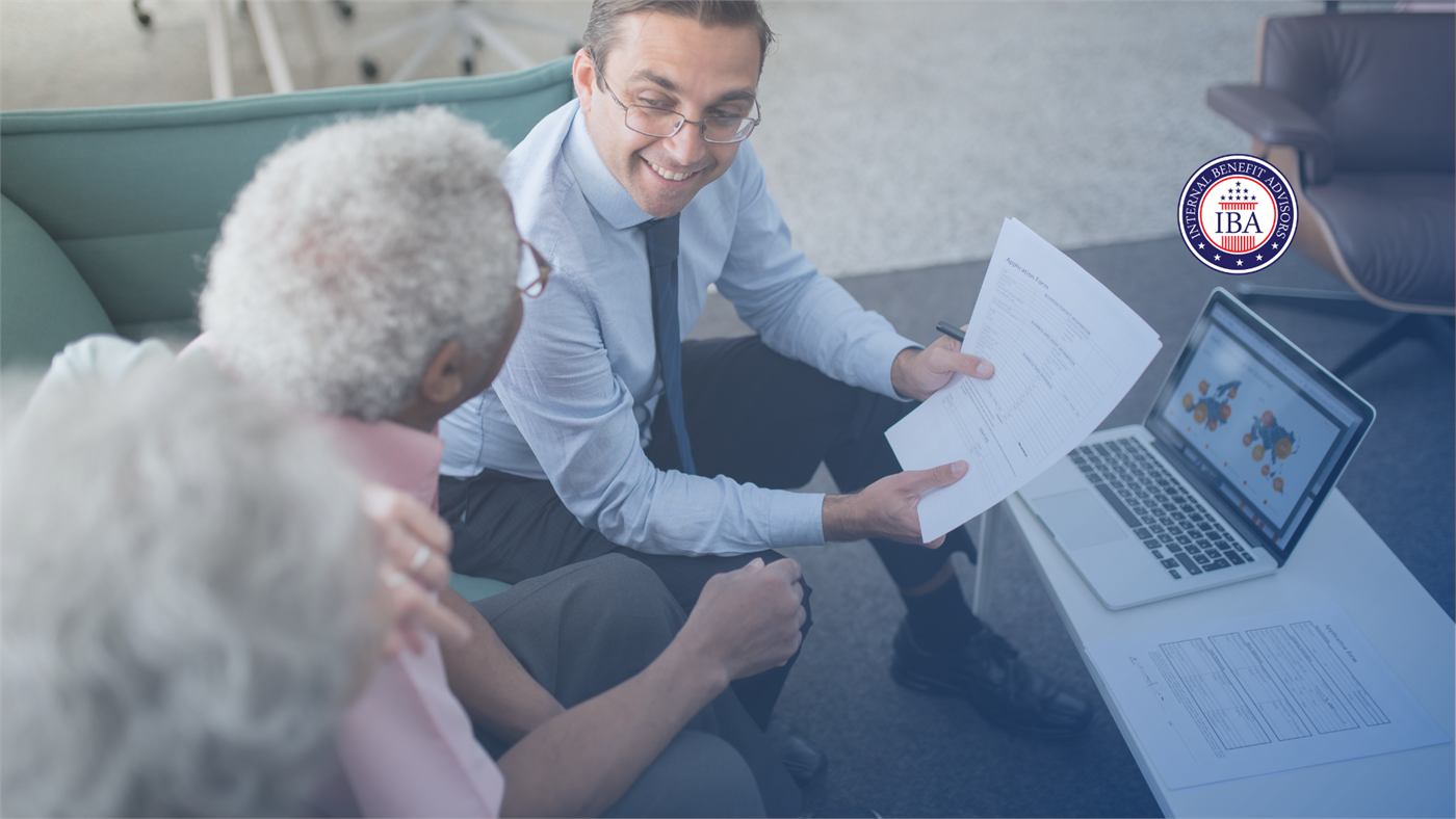 An adviser in a shirt and tie showing a printed document to an older couple, with an open laptop on the table