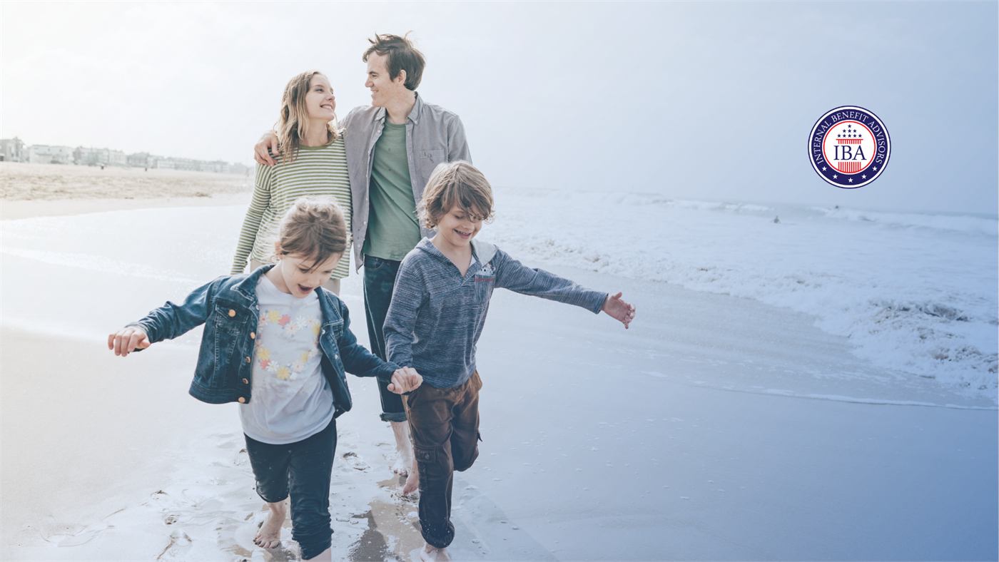A family of four walking barefoot along the shoreline of a wide beach