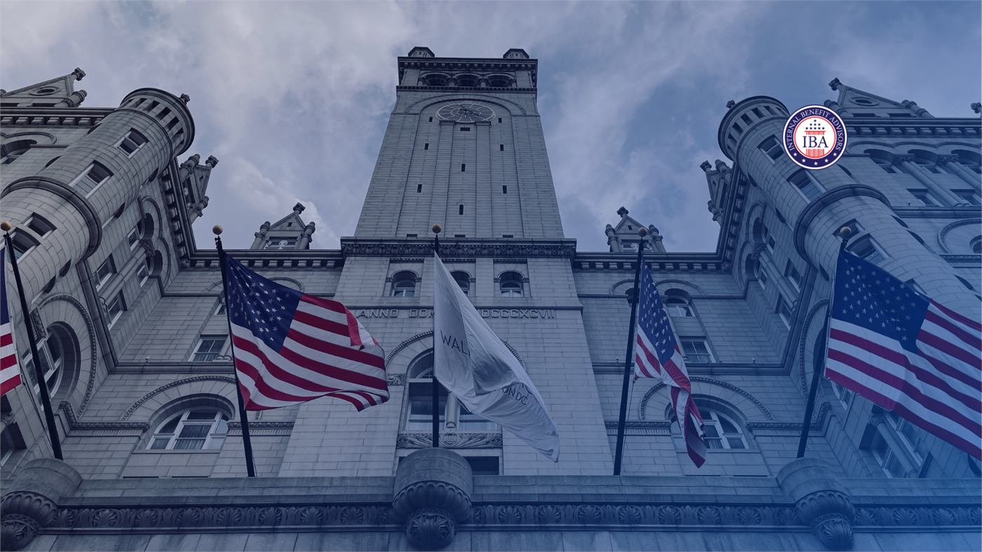 A grand stone government building with a clock tower, American flags flying along its facade