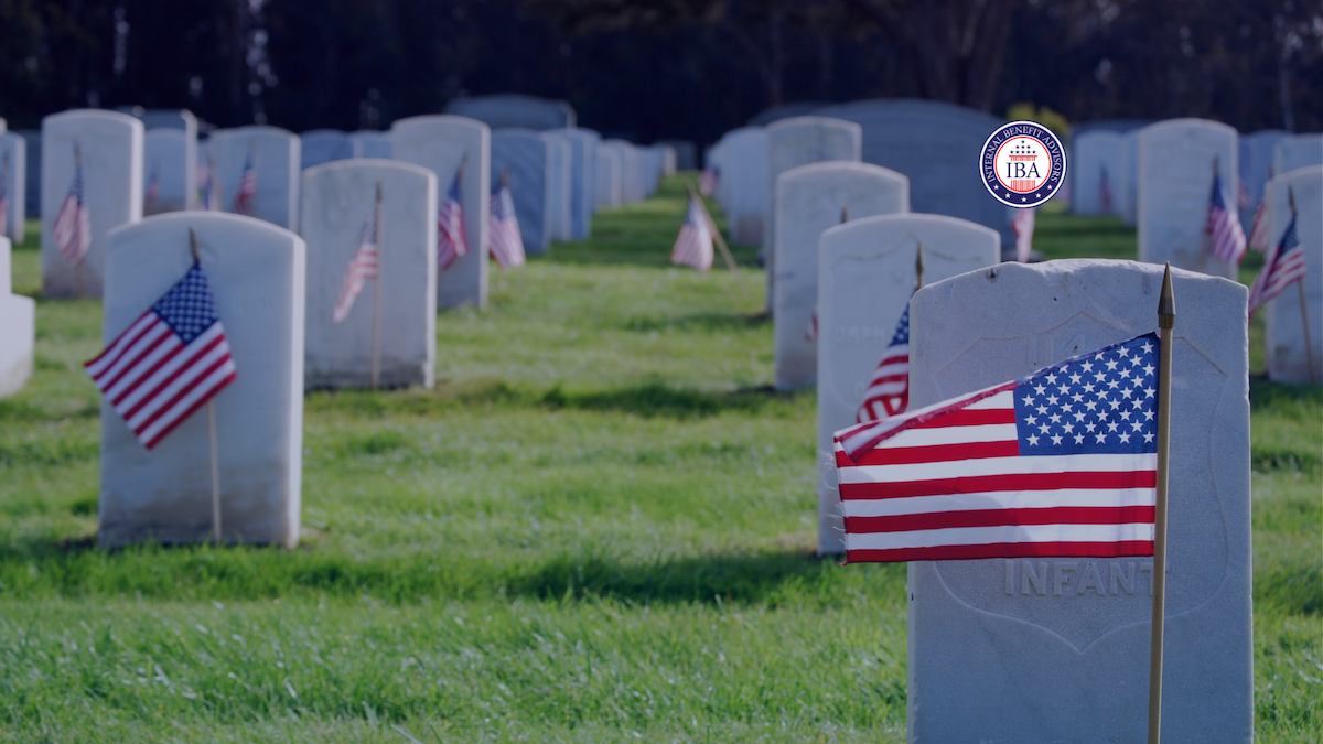 Rows of white headstones in a military cemetery, each marked with a small American flag