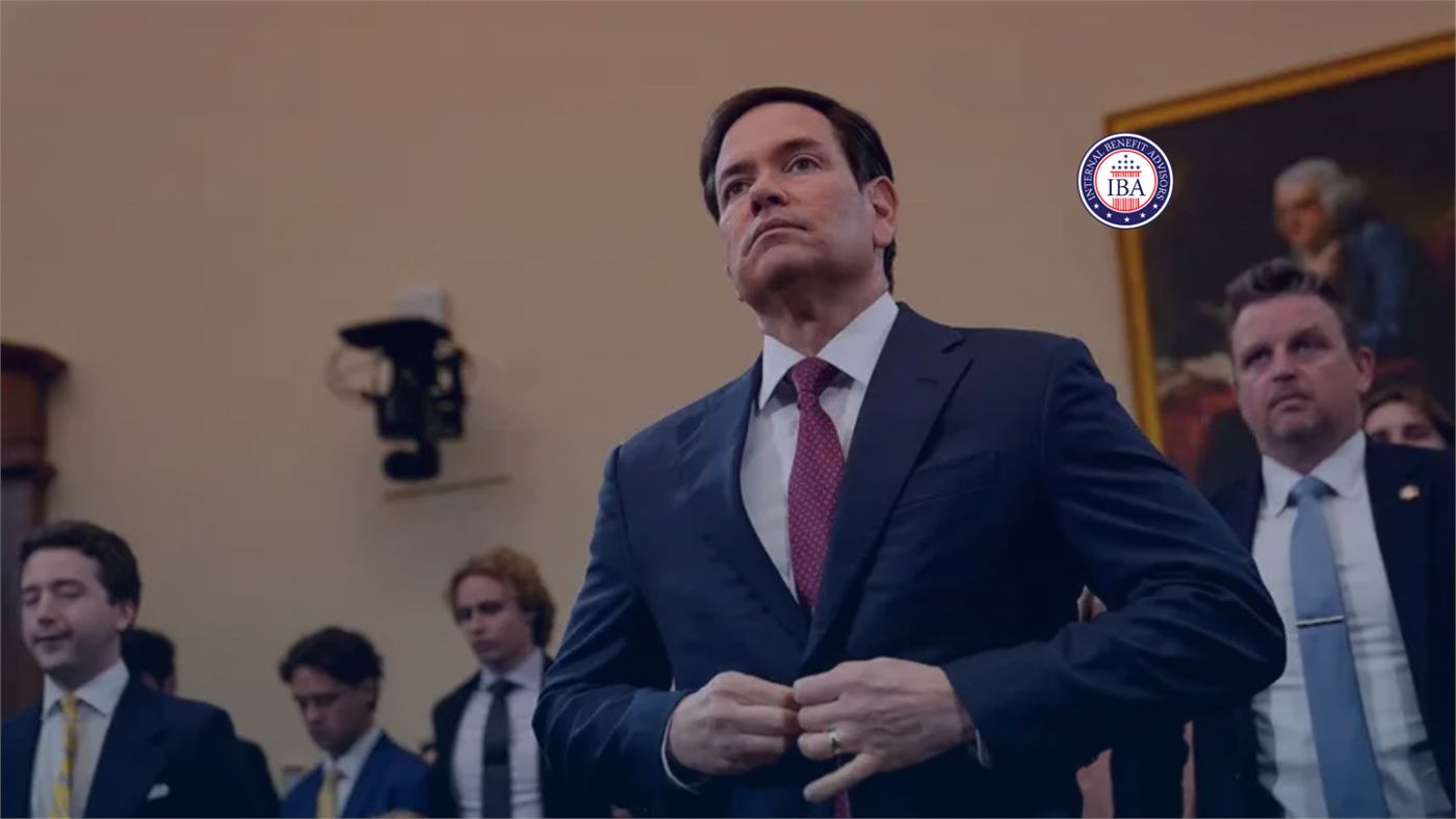 A government official in a dark suit walking past television cameras and aides