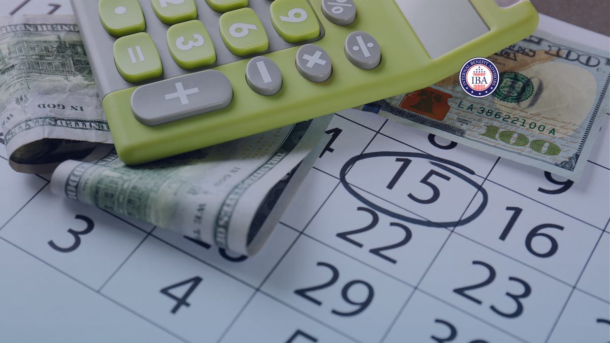 A green calculator and rolled banknotes resting on a calendar with the fifteenth circled