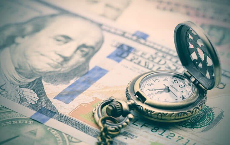 An antique pocket watch resting on a US hundred dollar bill