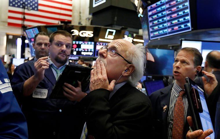 Traders reacting at a stock exchange floor, an American flag and market screens behind them