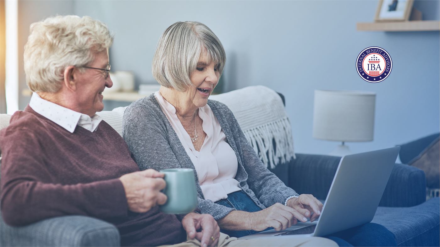 An older couple sitting together on a sofa with a laptop, holding mugs