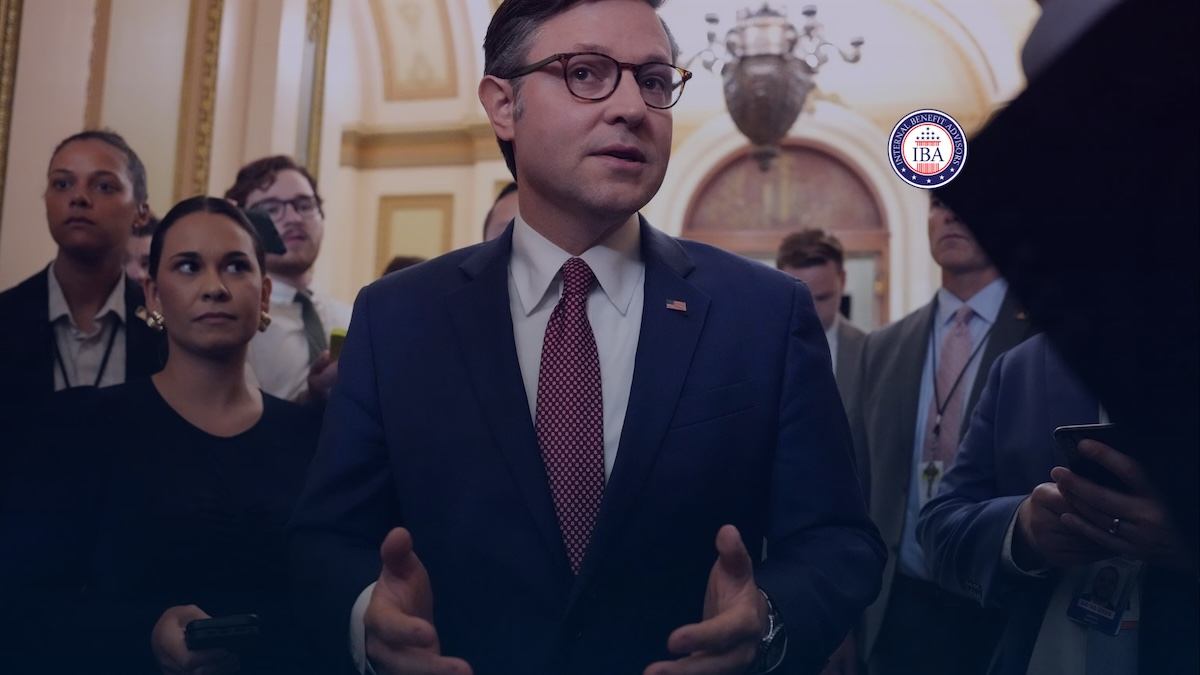 A man in a suit speaking to reporters in a marble corridor