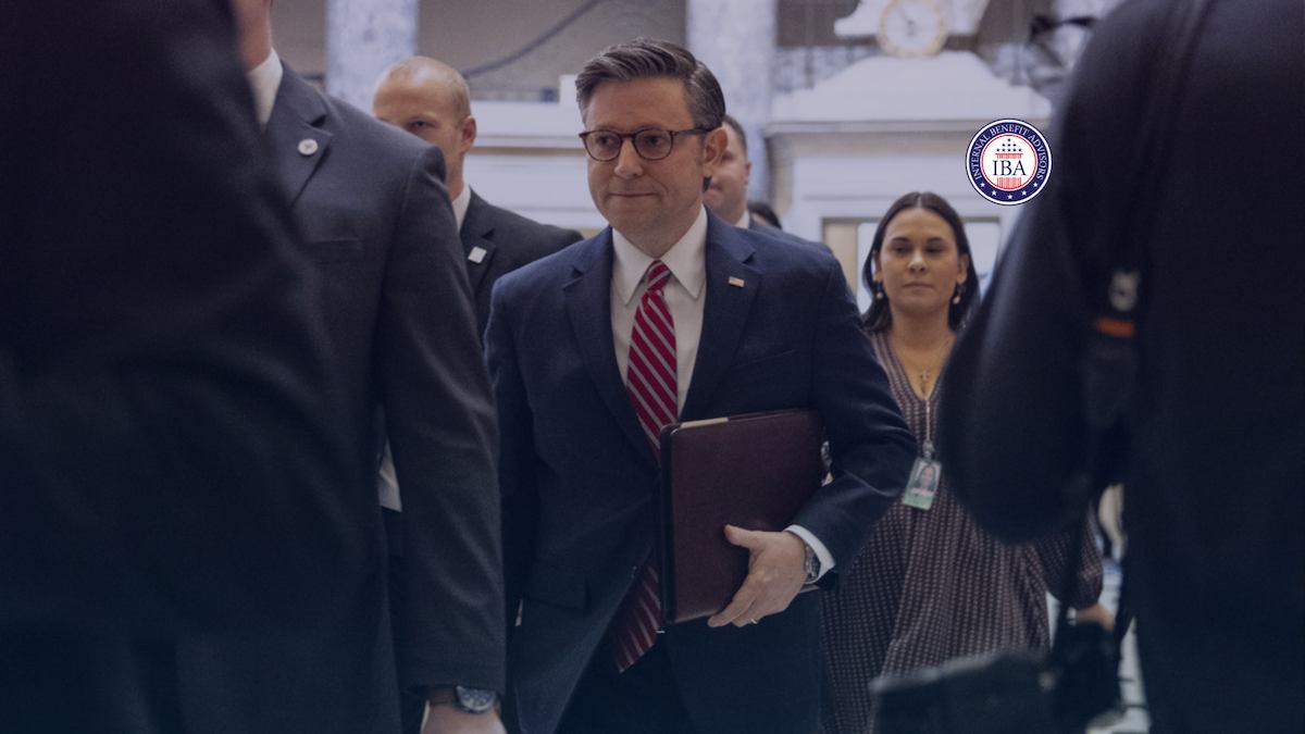 A man in a suit walking through a corridor accompanied by aides and reporters
