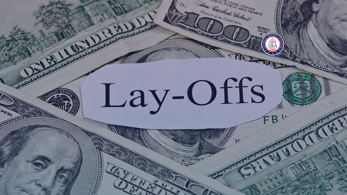 A paper cutting reading Lay-Offs resting on a pile of US hundred dollar bills