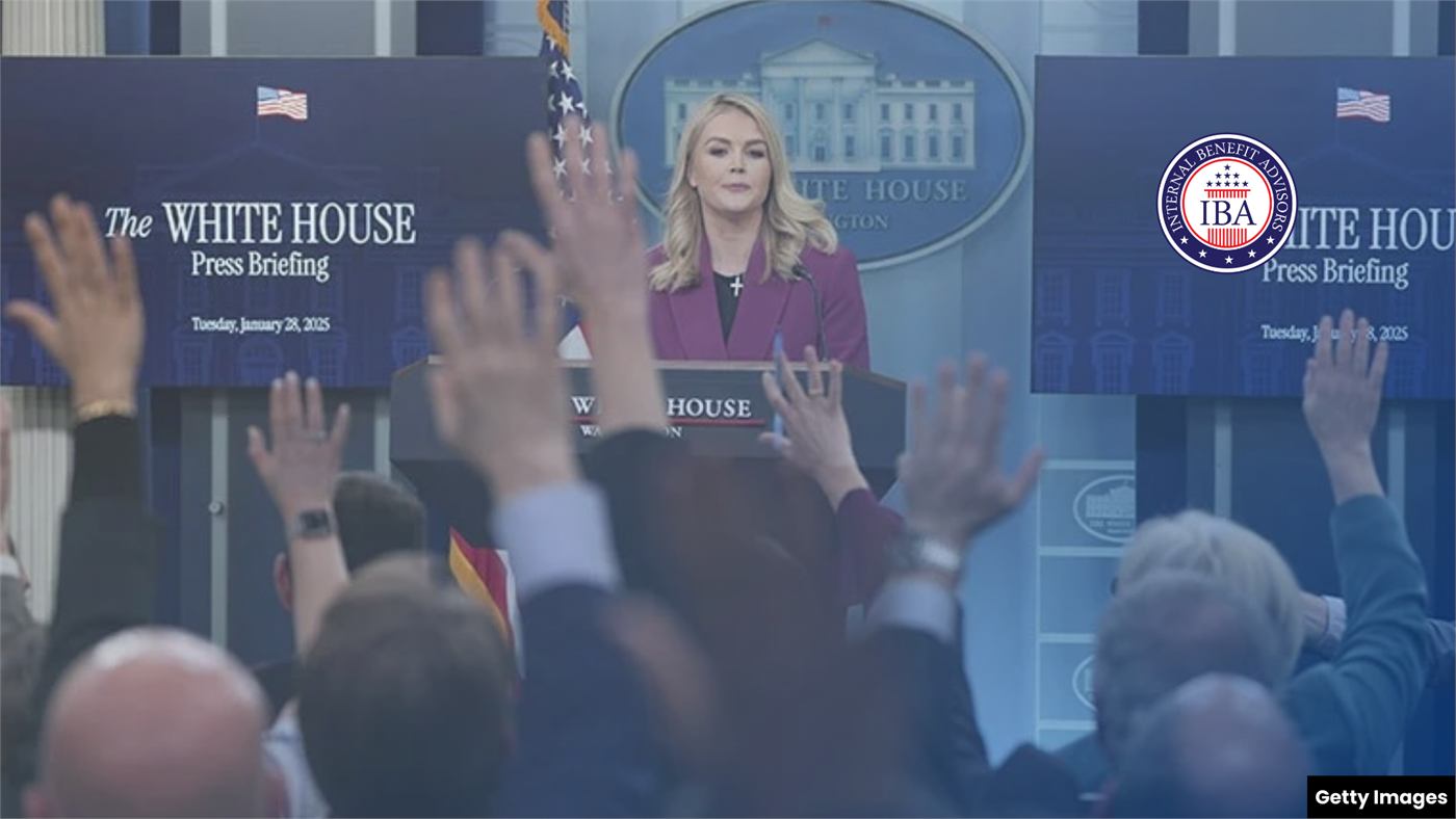 A White House press secretary at the briefing room podium as reporters raise their hands