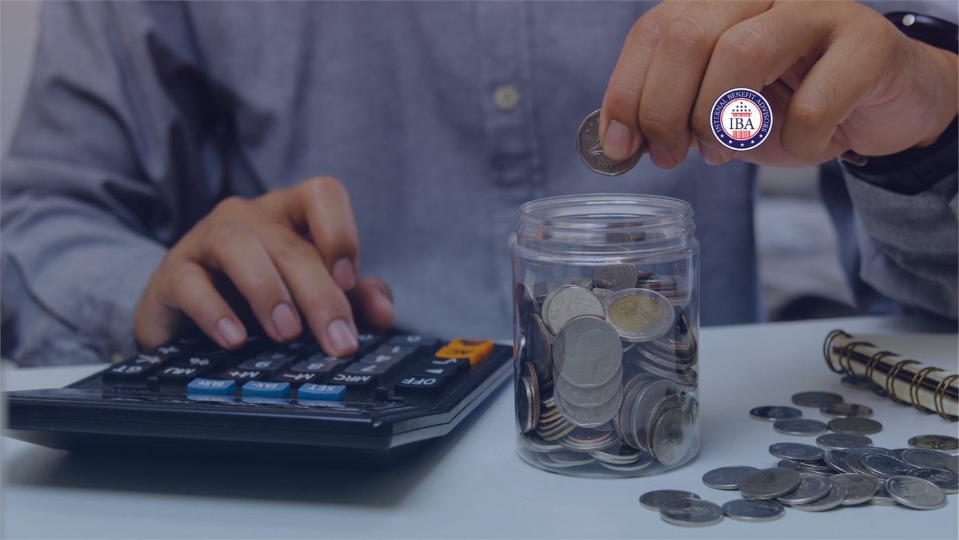 Hands using a calculator beside a jar of coins spilling onto a desk