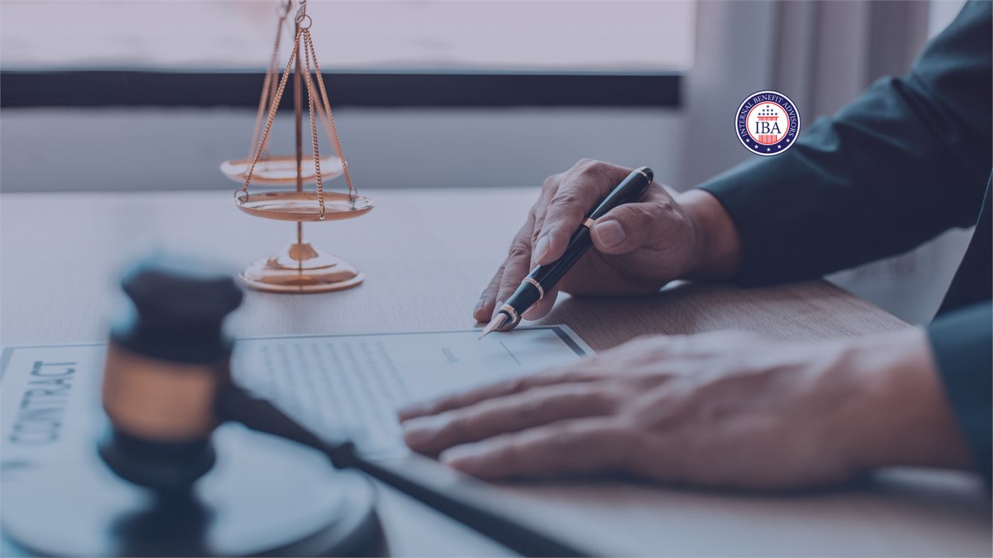 A hand signing a contract at a desk beside brass scales of justice and a gavel