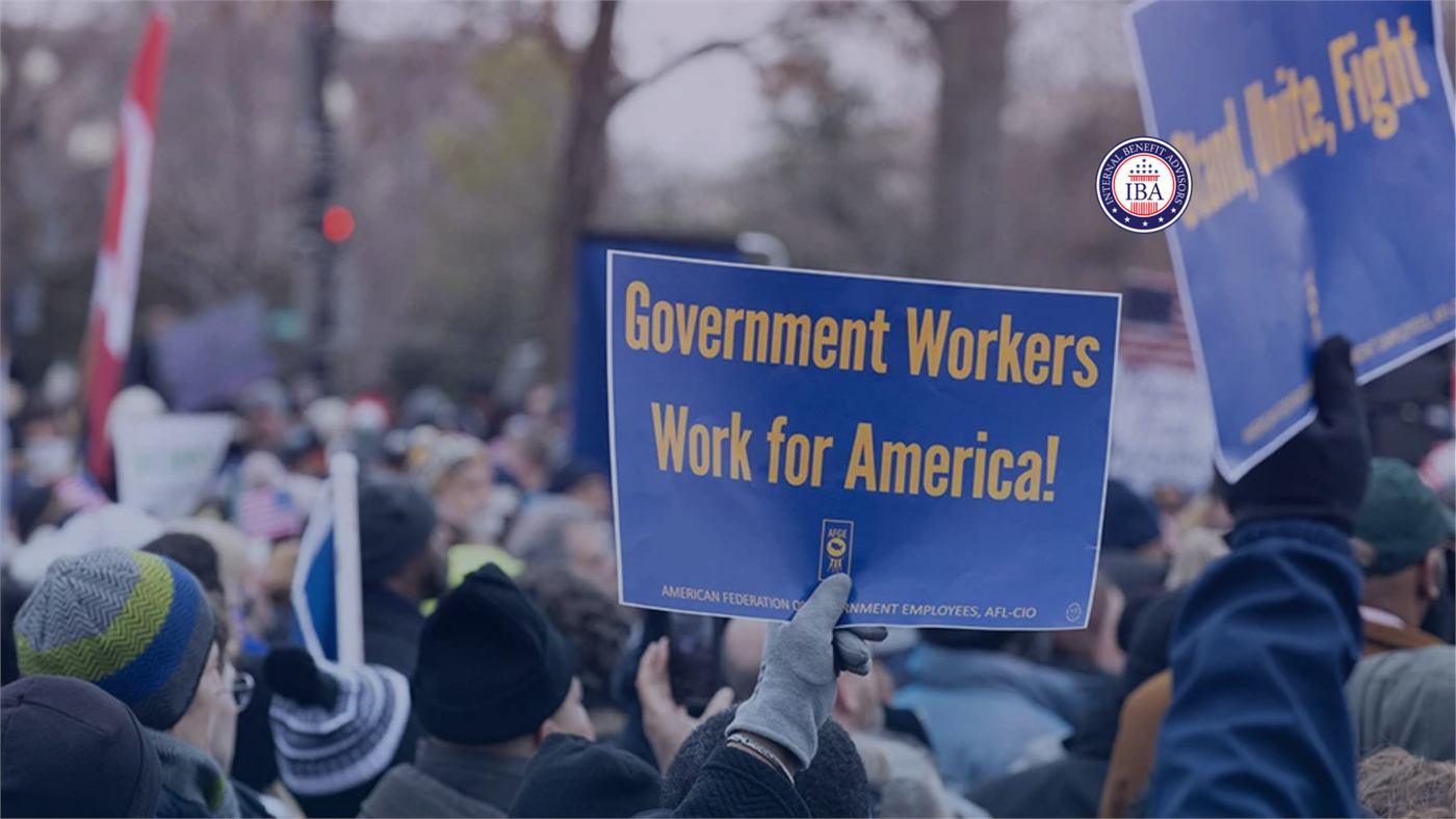 A crowd at a rally, one demonstrator holding a sign reading Government Workers Work for America