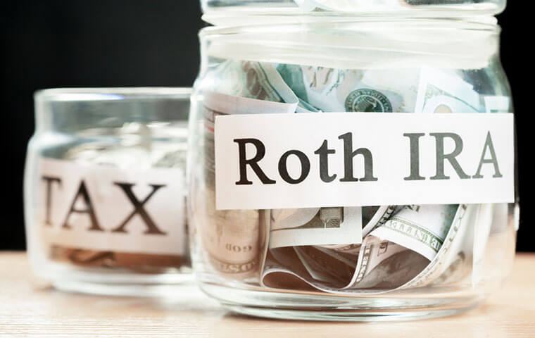 Two glass jars labelled Tax and Roth IRA, the Roth jar filled with banknotes