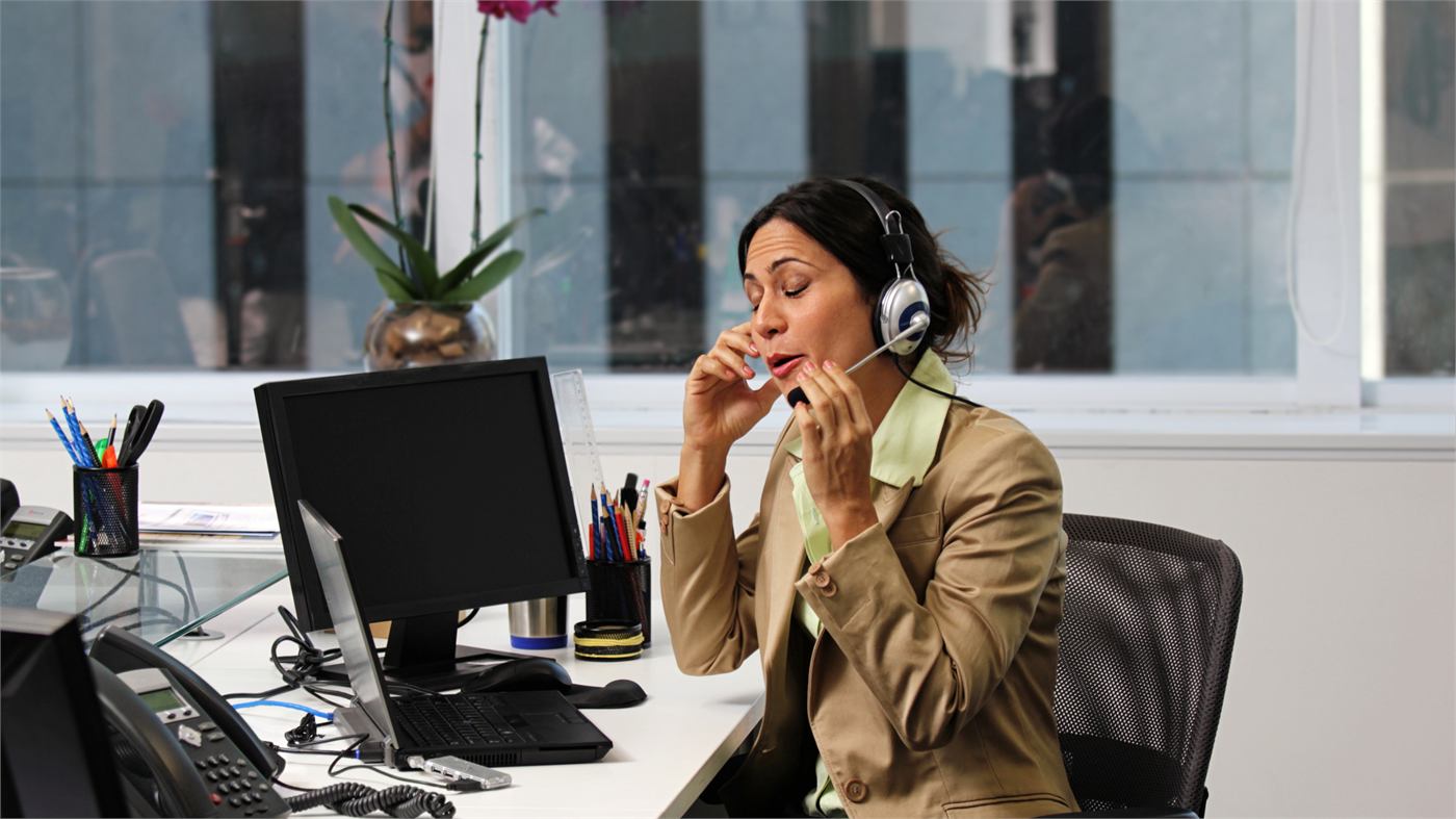 A woman wearing a headset taking a call at an office desk